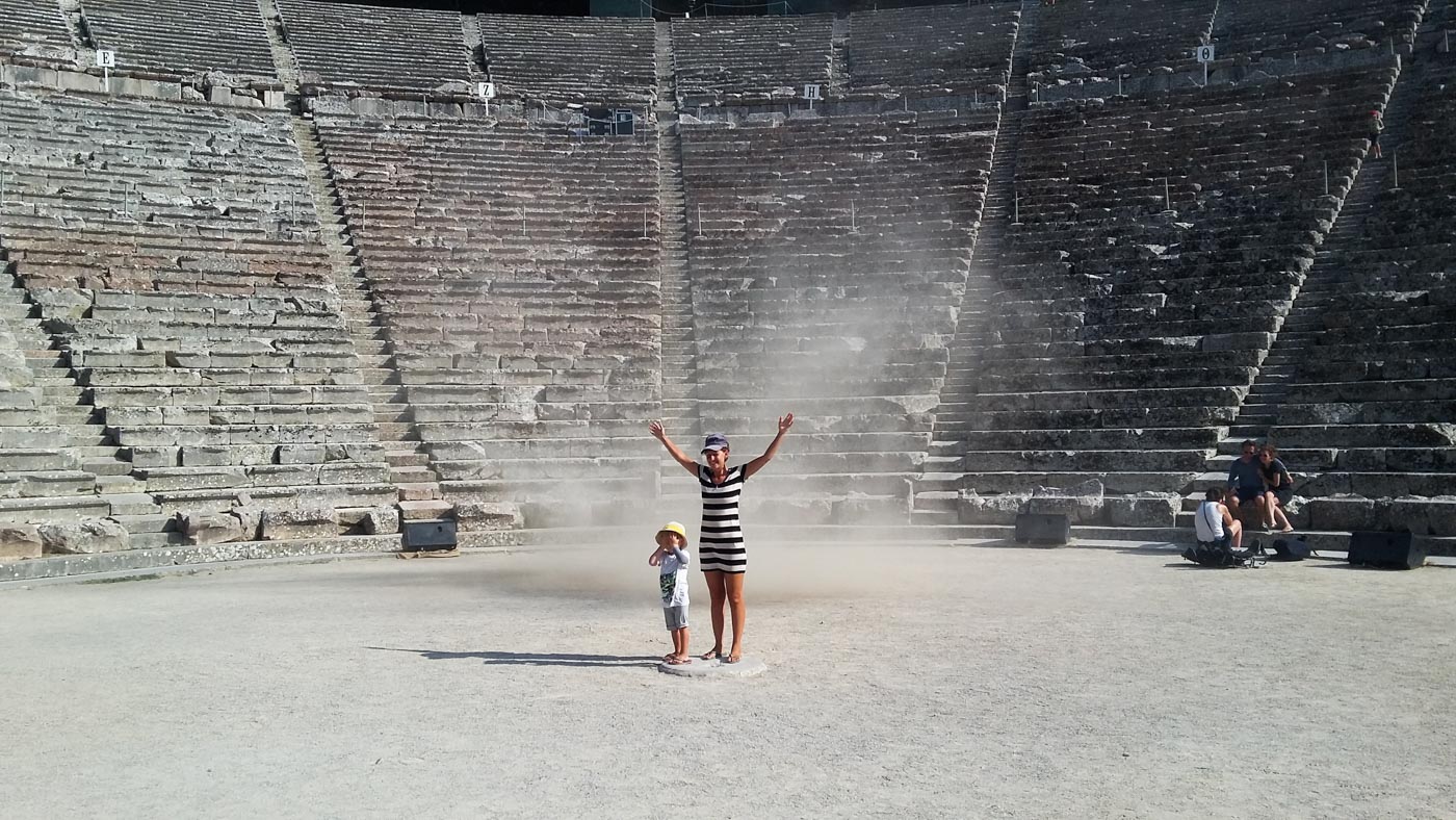 Lea und Luk stehen genau im Zentrum des Amphitheaters in Epidauros. Hinter ihnen zieht eine kleine Windhose vorbei