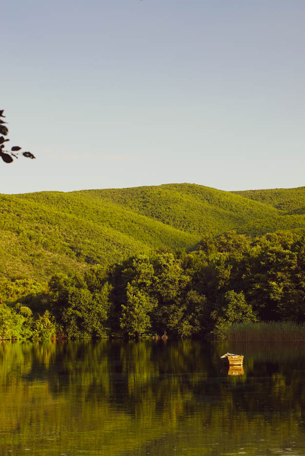 Es ist ein kleiner See zu sehen in dem sich die grünen Hügel im Hintergrund spiegeln, auf ihm schwimmt ein einzelnes altes Holz Ruderboot