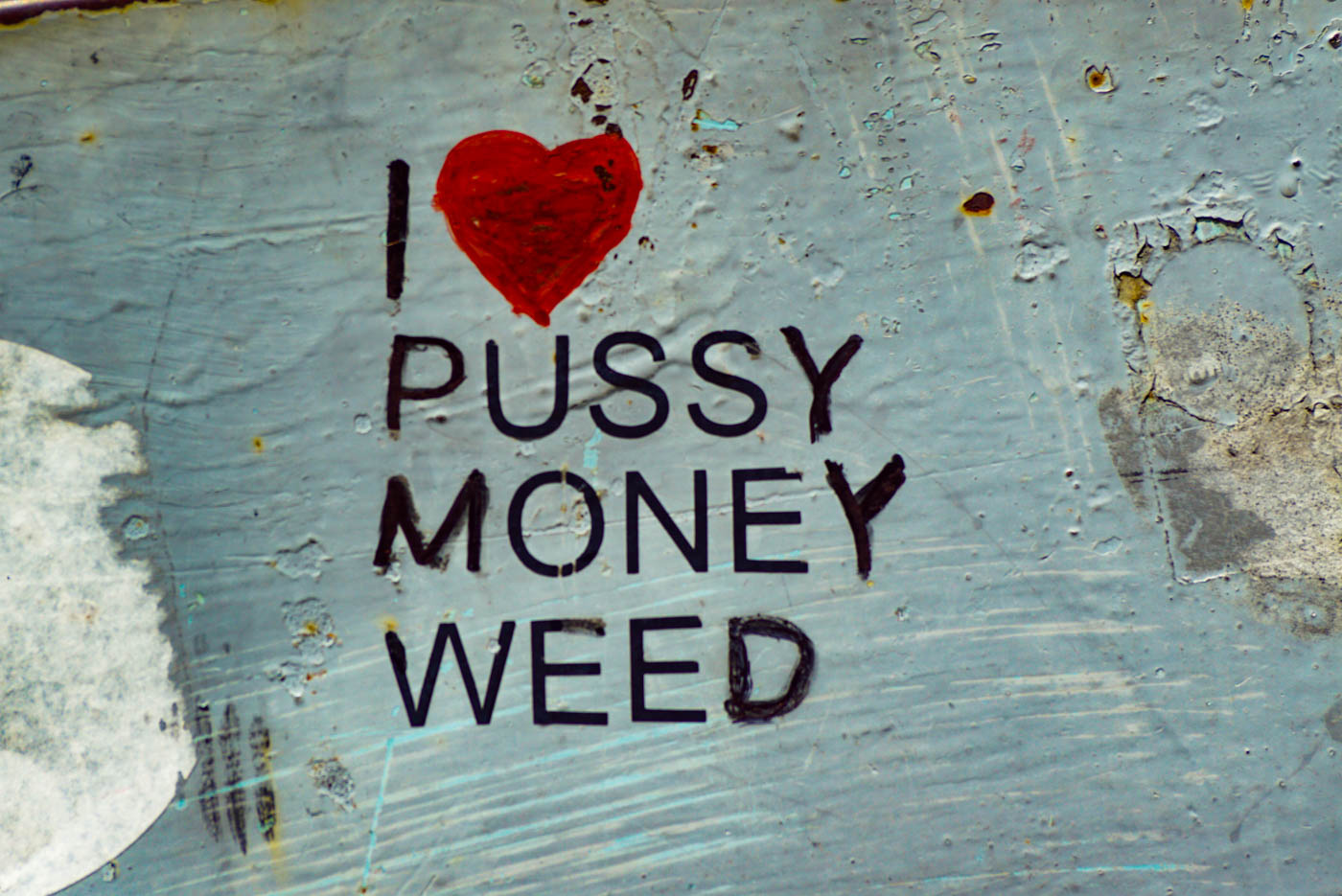 Es ist eine verwitterte Wand zu sehen mit der Aufschrift I Herzchen Pussy Money Weed