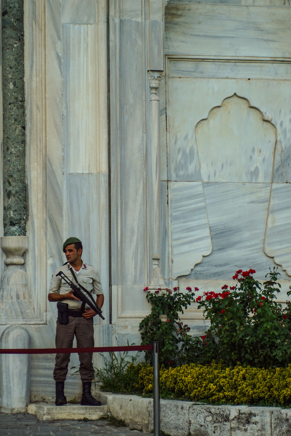 Das Bild zeigt einen Wachmann in der Nähe der Hagia Sophia wie er nach rechts guckt. Dadurch sind die zwei Männer die vor dem secondhand BH Laden sitzen von den Soldaten eingerahmt die sie beobachten.