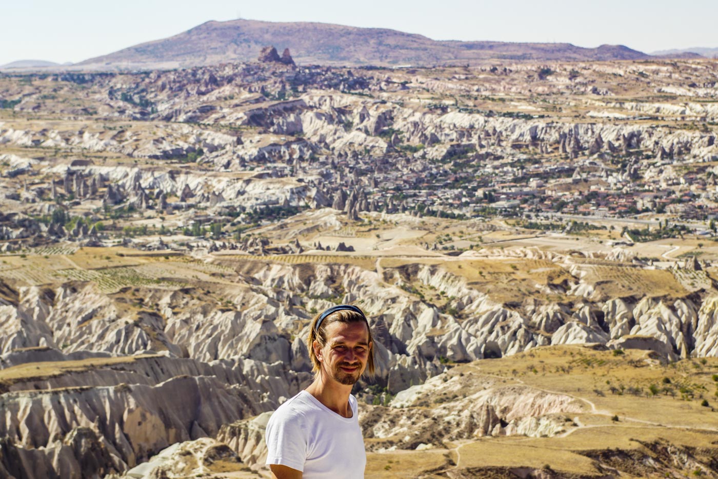 Paul steht auf einem Berg und blickt in die Kamera im Hintergrund ist die wunderschöne zerfurchte kappadokische Landschaft mit ihren Zuckerhüten und Tälern zu erblicken.