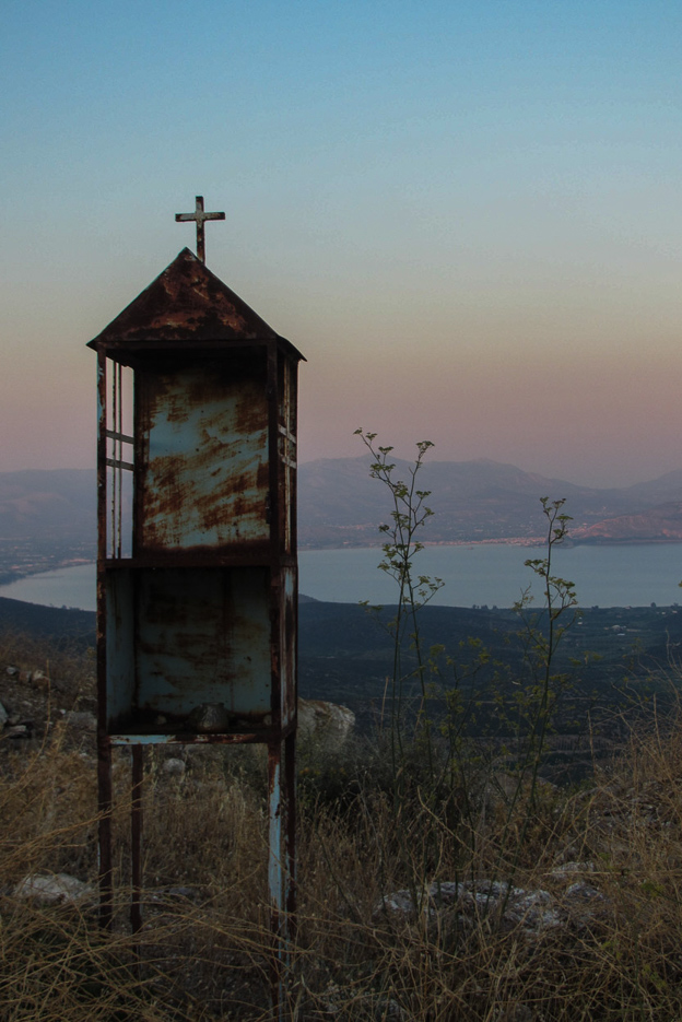 Im Vordergrund steht ein griechisch-orthodoxes Andenken schreien im Hintergrund erstreckt sich eine Bucht mit Bergen